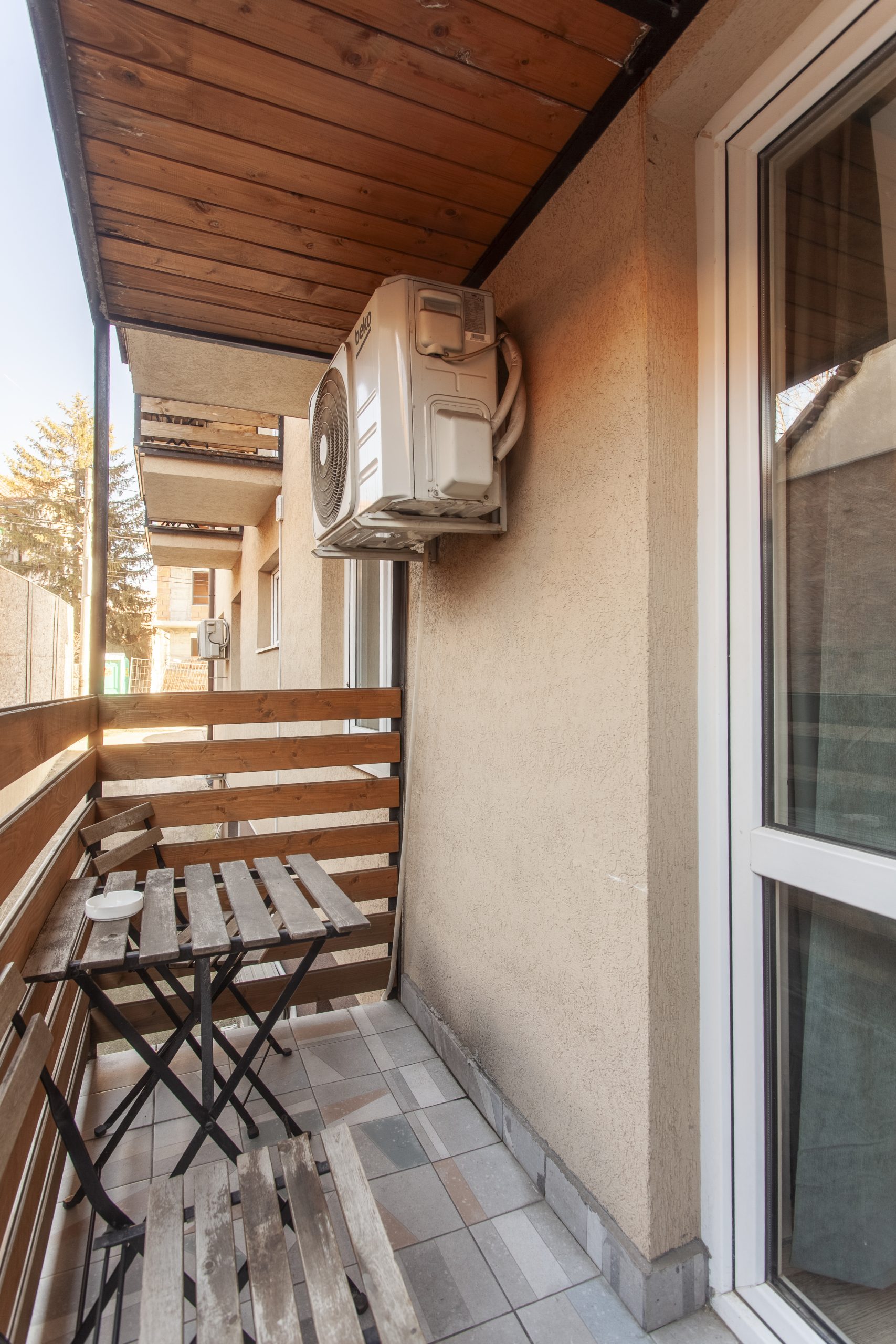 Fotografija prikazuje balkon sa stolom i stolicama, klima uređa