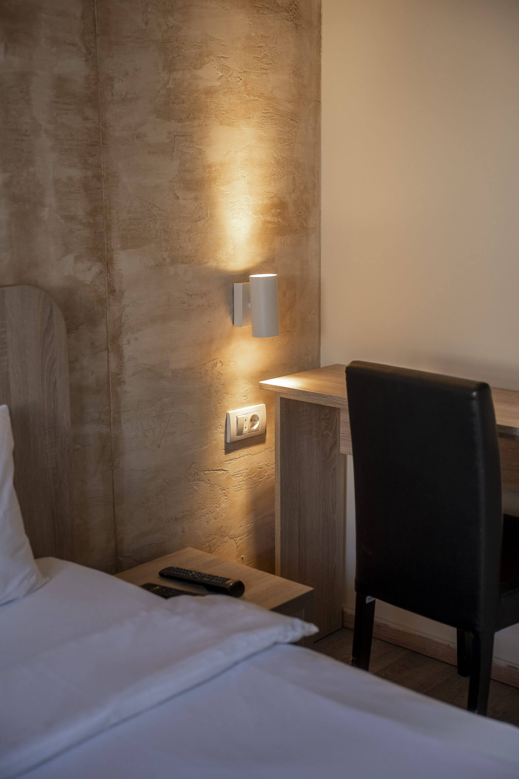 Fotografija prikazuje deo sobe sa krevetom, radnim stolom i lamp